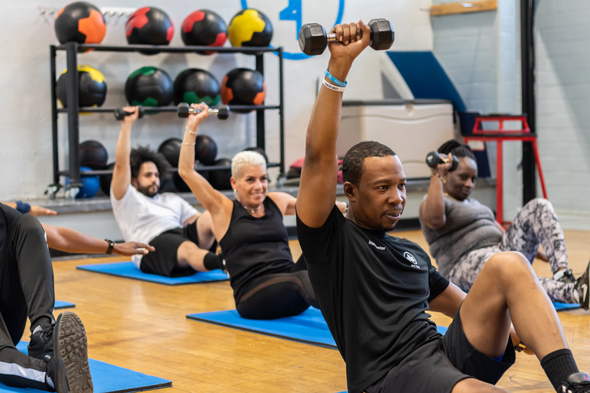 A group lays on exercise mats with a dumbbell over their heads.