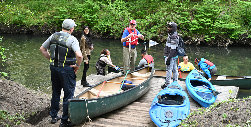 A group of people getting into a canoe on a river while others wait on the pier. A canoe and two kayaks are sitting on the pier, ready to go into the water. 